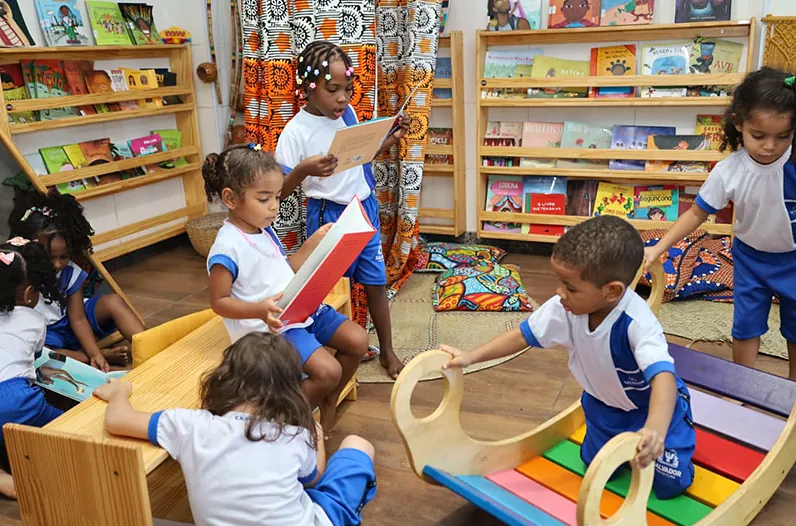 Crianças da educação infantil lendo livros e brincando no cantinho de leitura da escola